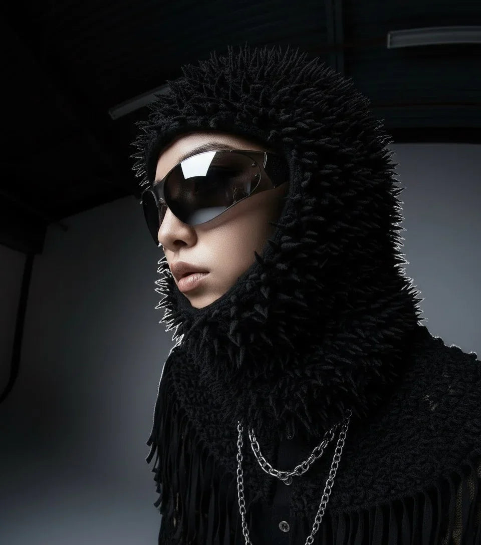 Model in spiked black hood, dark sunglasses, chain necklace, sharp opium fashion style