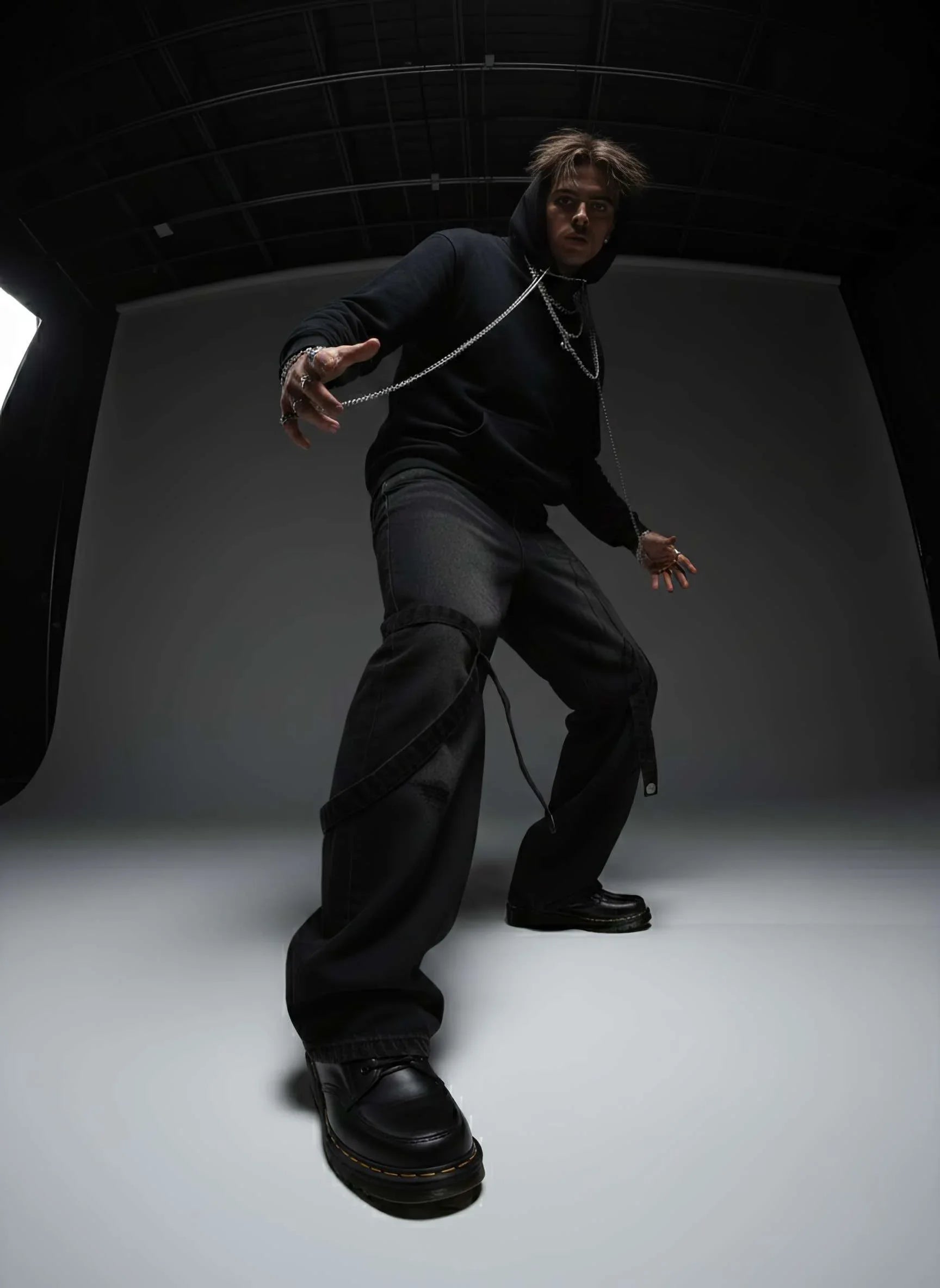 Person in black outfit with a white rope around their neck against a dark background